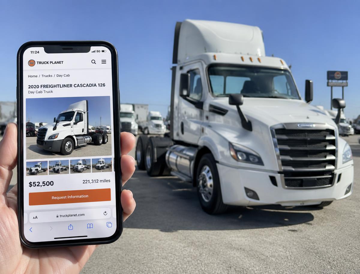 Phone showing a semi truck listed for sale online, with the same truck on the lot behind it